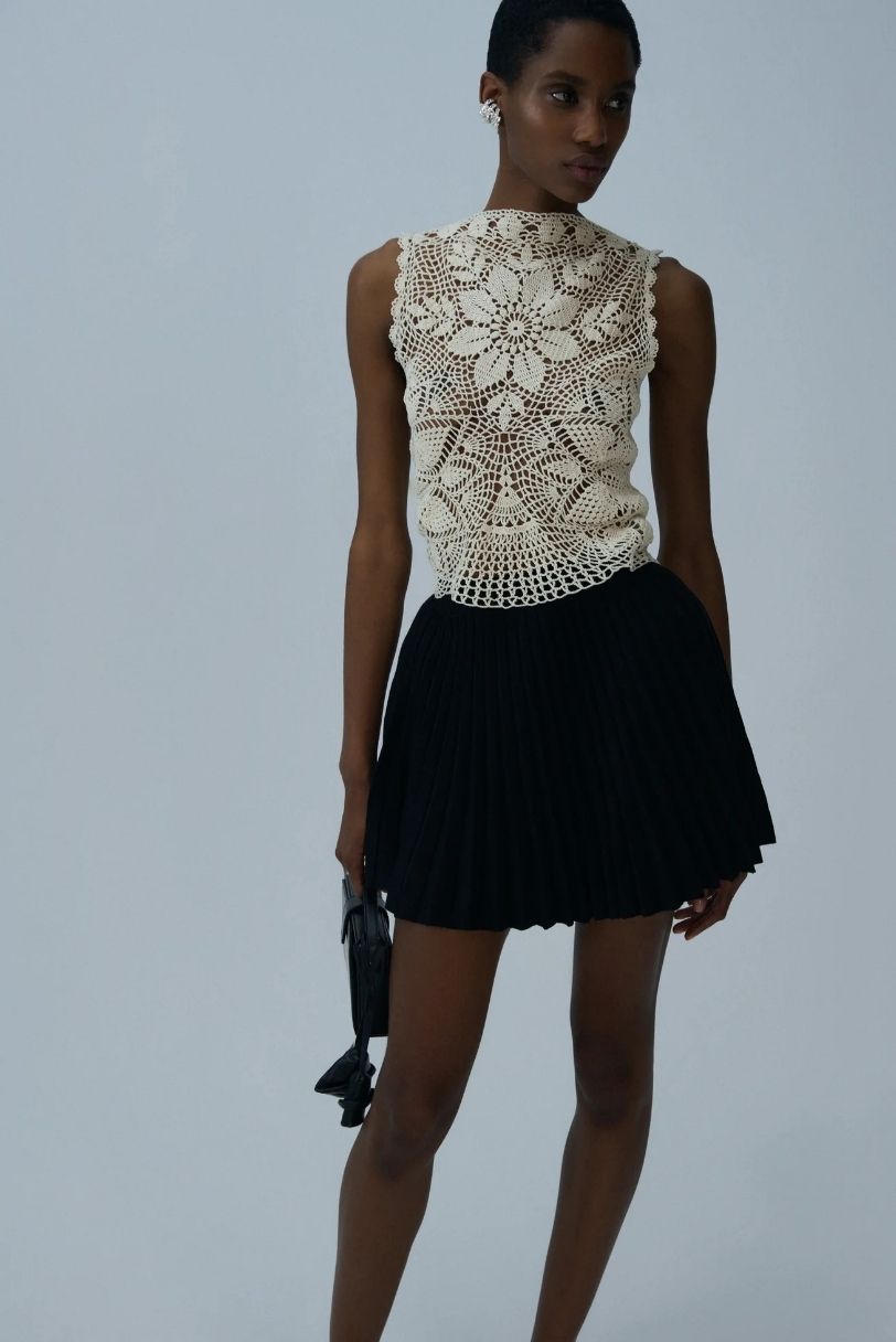Top de crochet bege com flores vazadas combinado com saia curta preta plissada