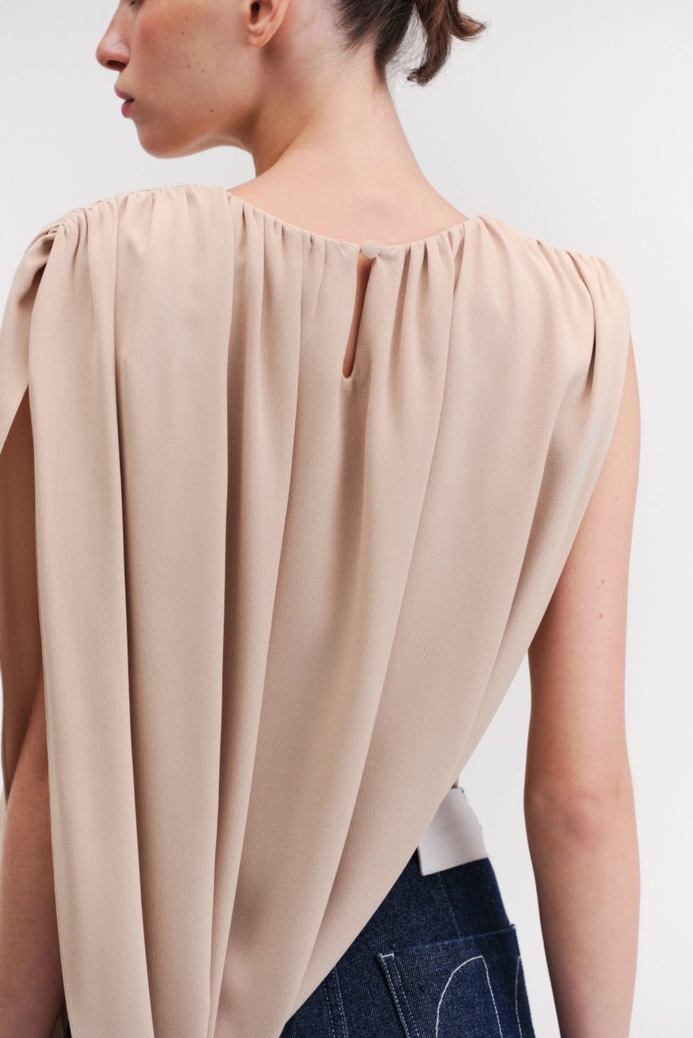 Detalhe das costas da blusa bege com pregas suaves e fechamento posterior