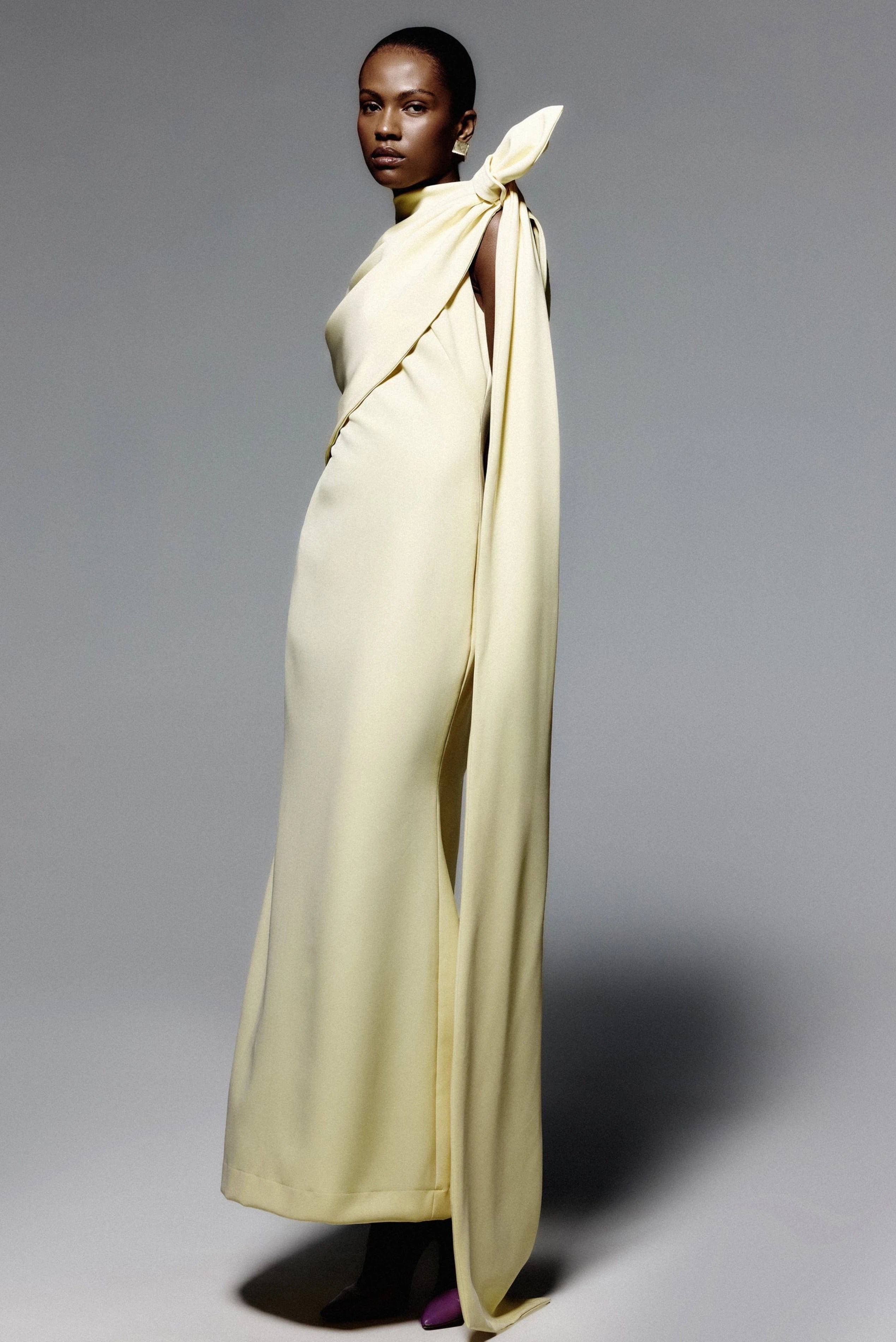 Vestido de festa amarelo-claro com capa drapeada, gola alta e detalhe de laço lateral