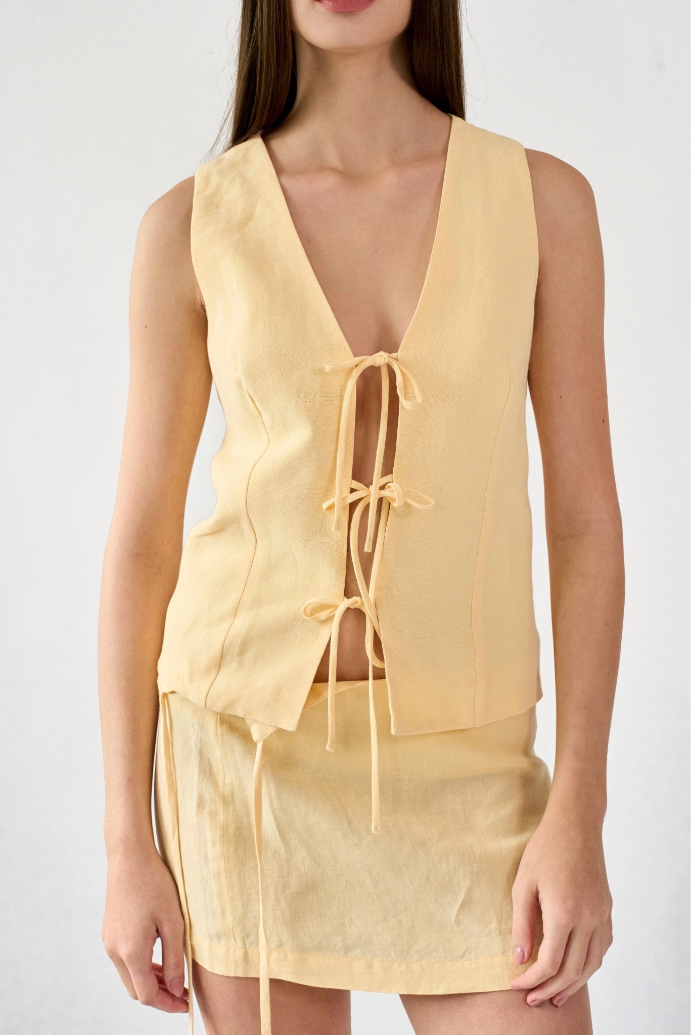 Close do Colete Mia MR em linho amarelo claro com amarrações frontais e caimento reto