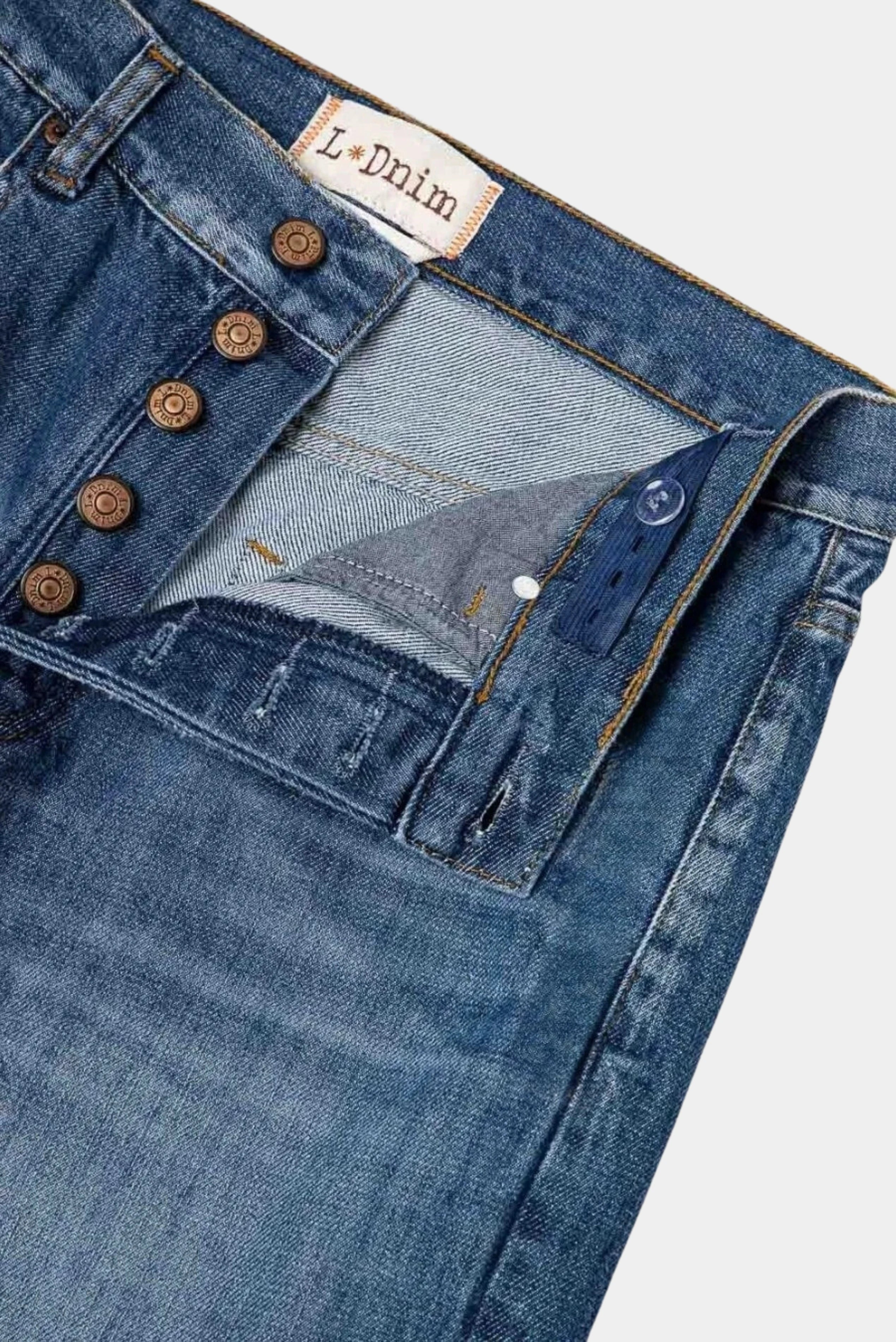 Detalhe interno da calça jeans azul com fechamento por botões e acabamento em denim.