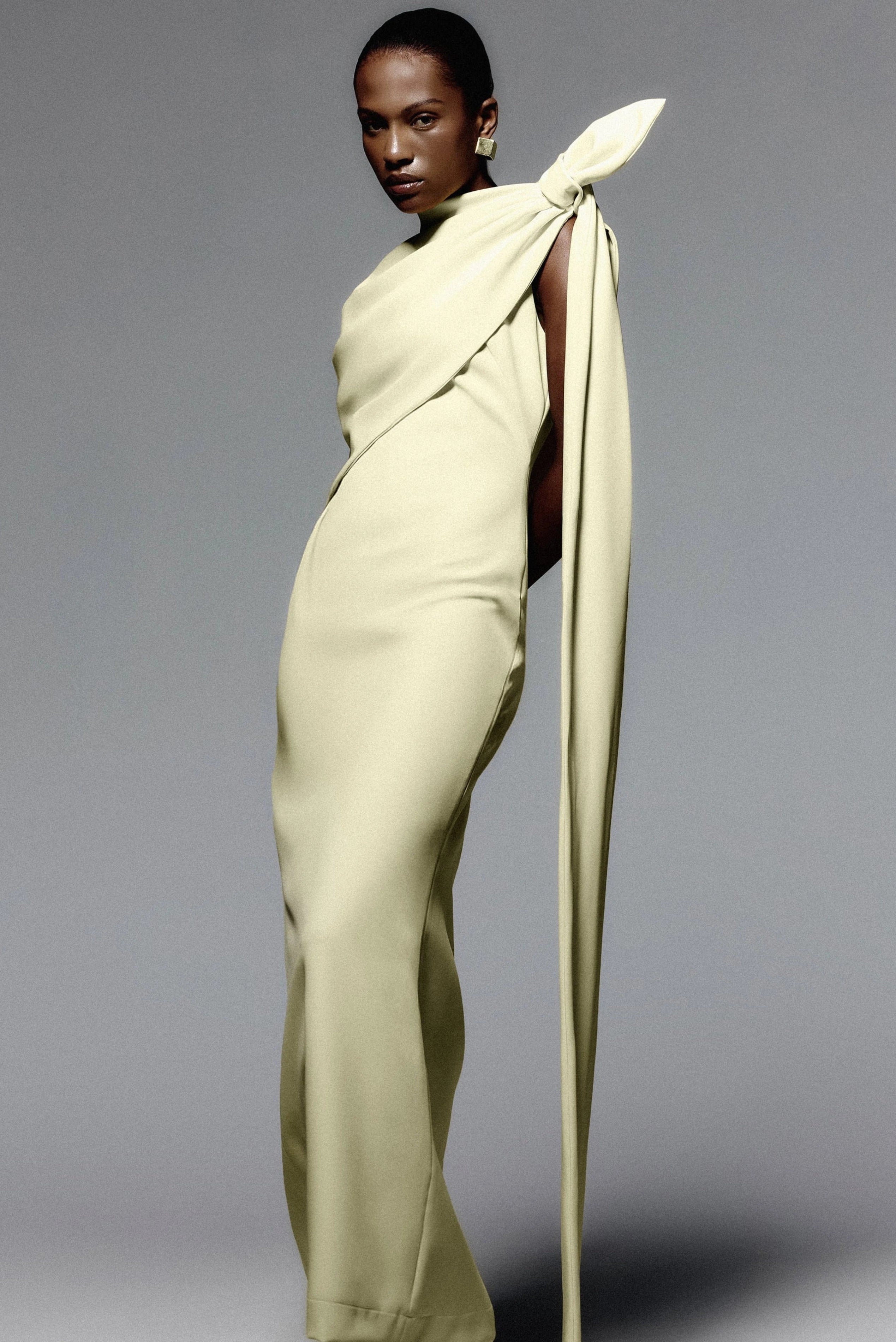 Vestido minimalista amarelo-claro com capa drapeada e faixa longa em modelagem elegante