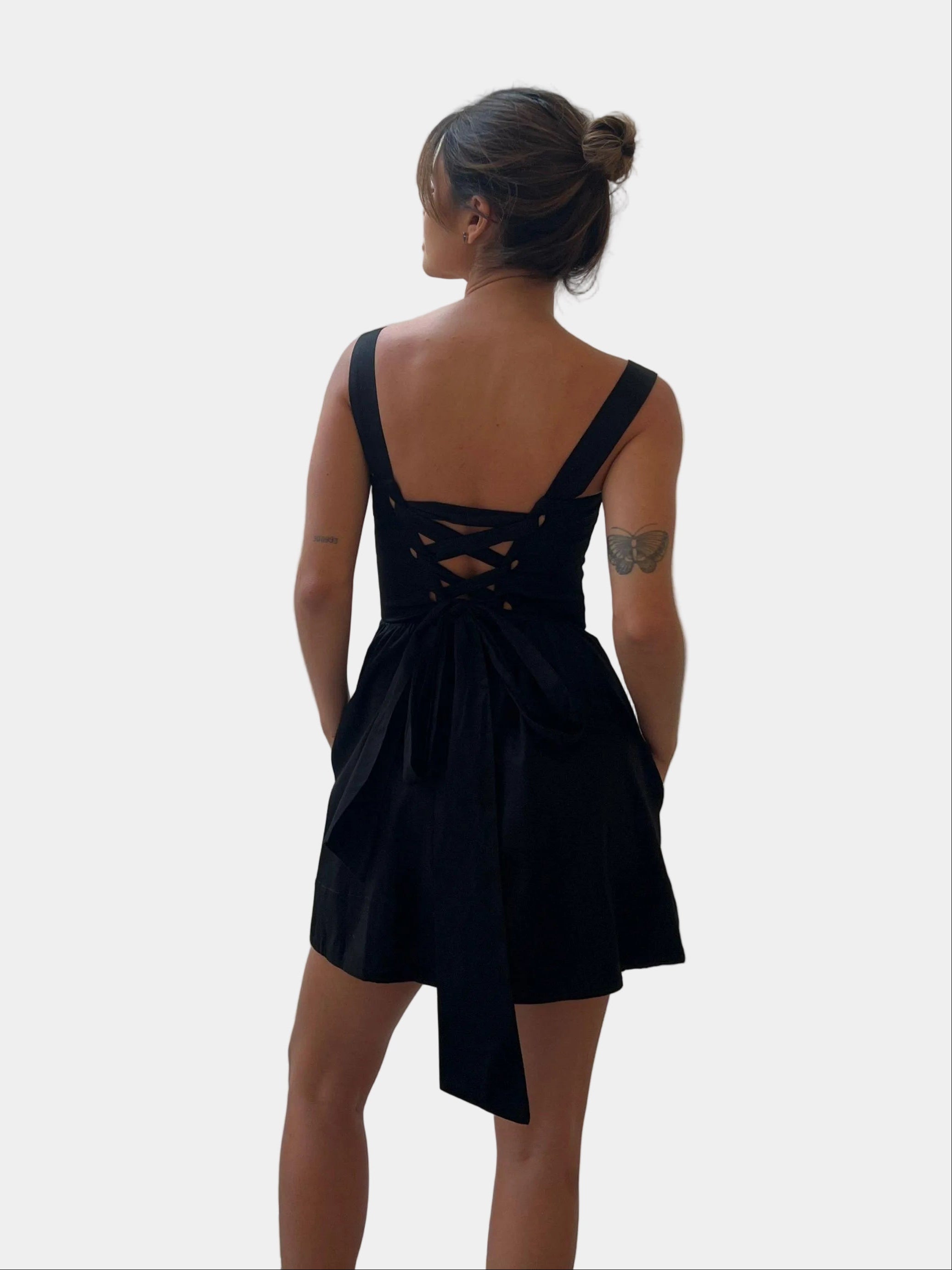 Modelo com vestido curto preto de costas com amarração cruzada e laço posterior