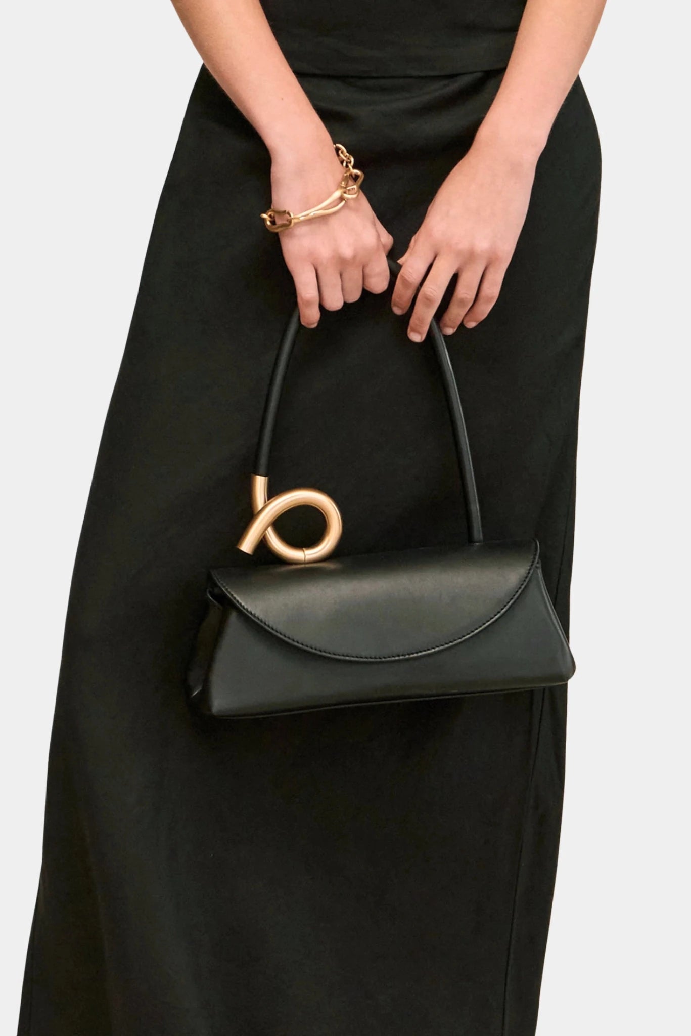 Close da bolsa Cult Gaia preta com acabamento liso e alça escultural dourada