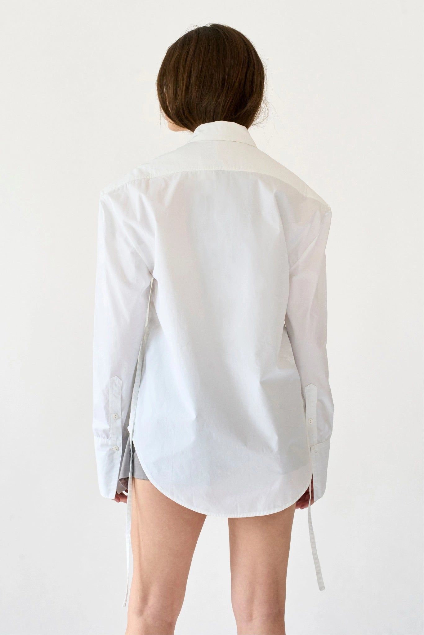 Costas da camisa Yuka MR branca com caimento alongado e detalhe de amarração