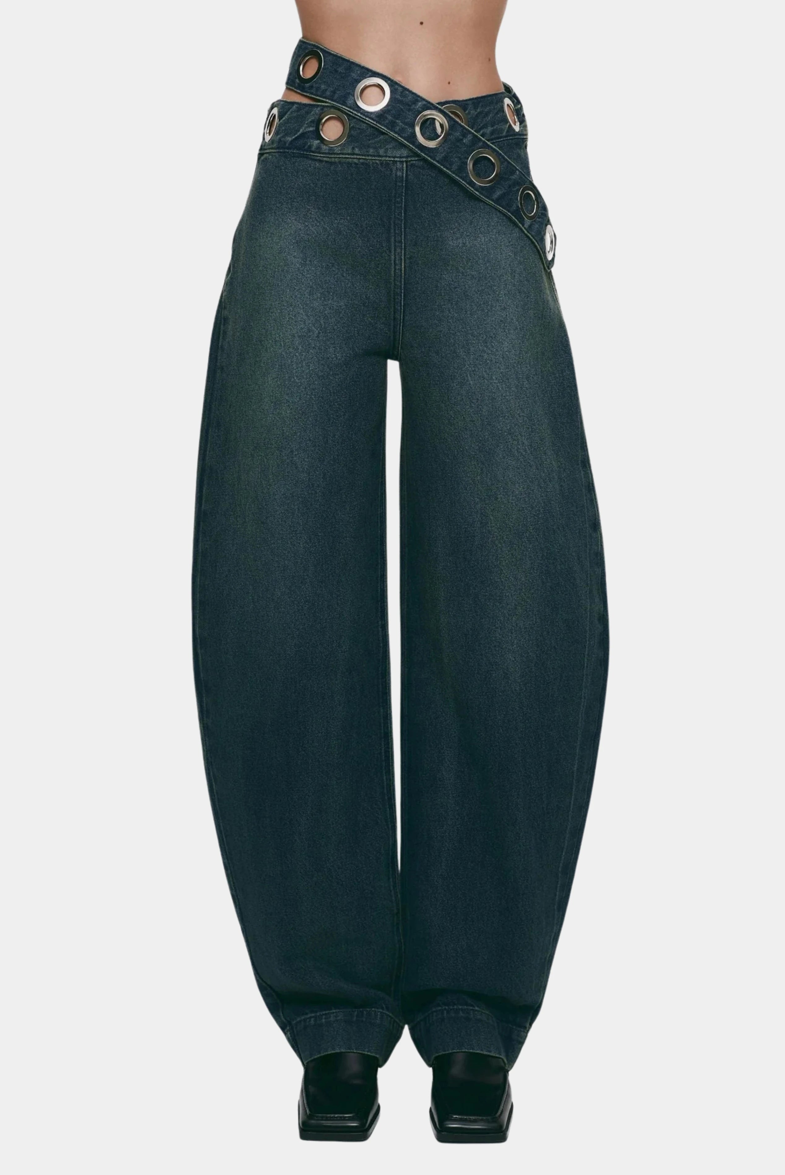 Detalhe frontal da calça jeans azul escuro com cós assimétrico e aplicação de ilhoses metálicos