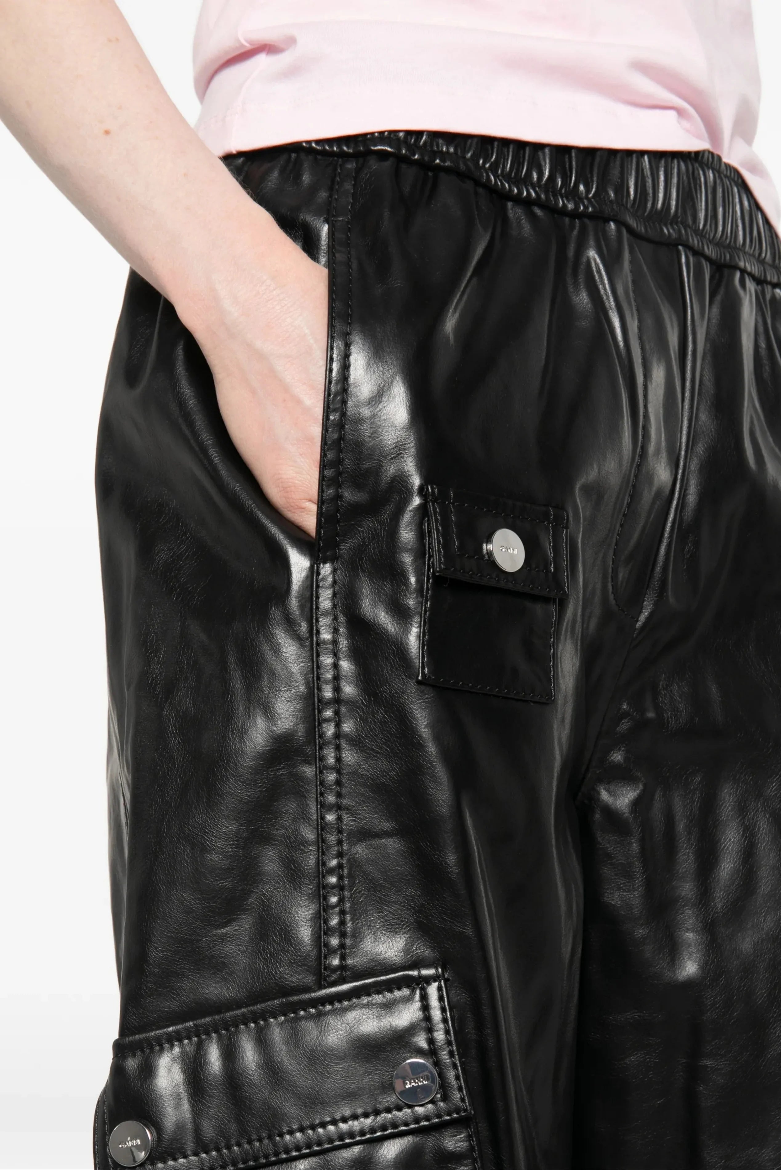Modelo usando calça cargo preta em couro Ganni com bolsos laterais e caimento amplo