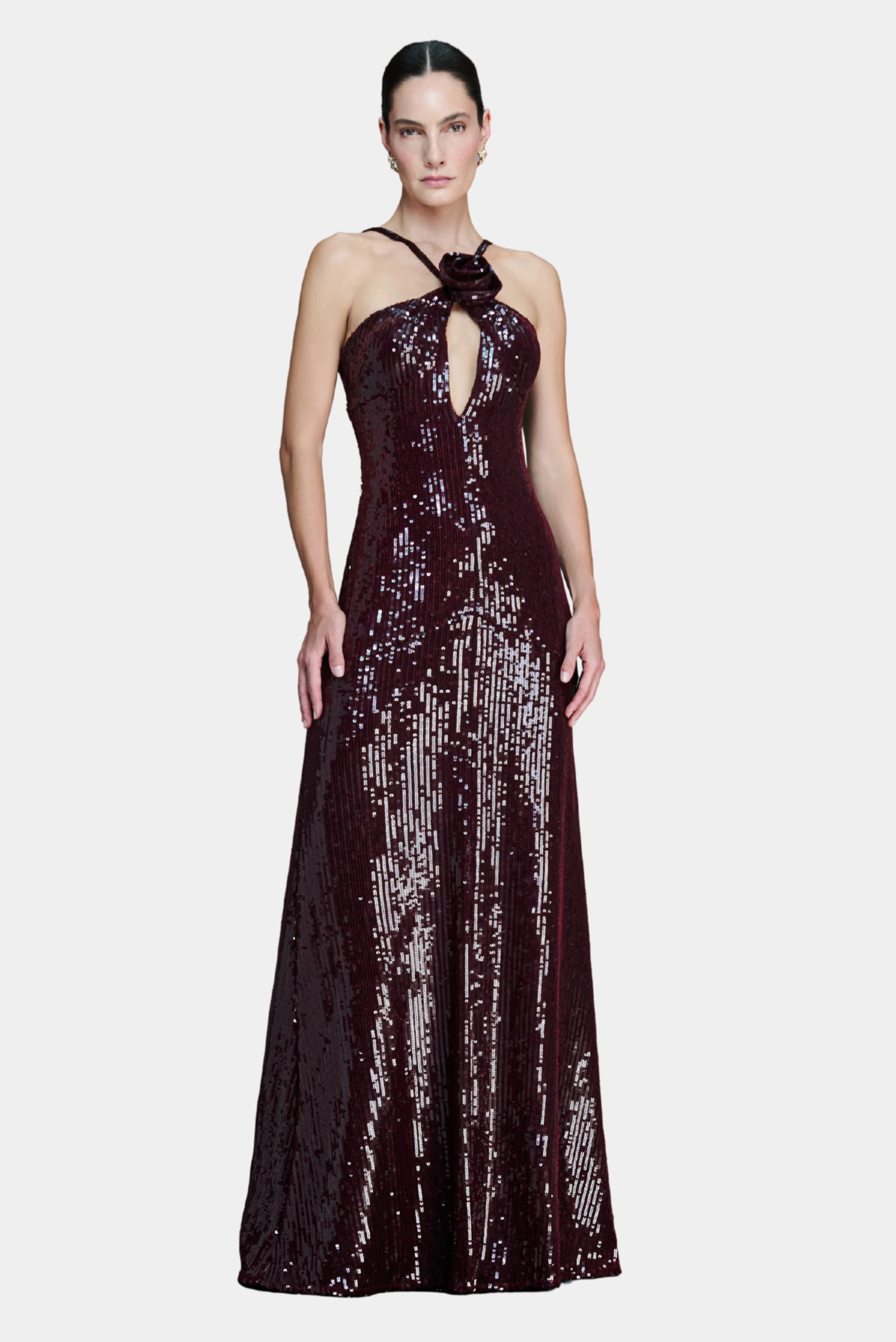 Modelo veste vestido longo vinho em paetês com decote halter, recorte frontal e detalhe floral na gola