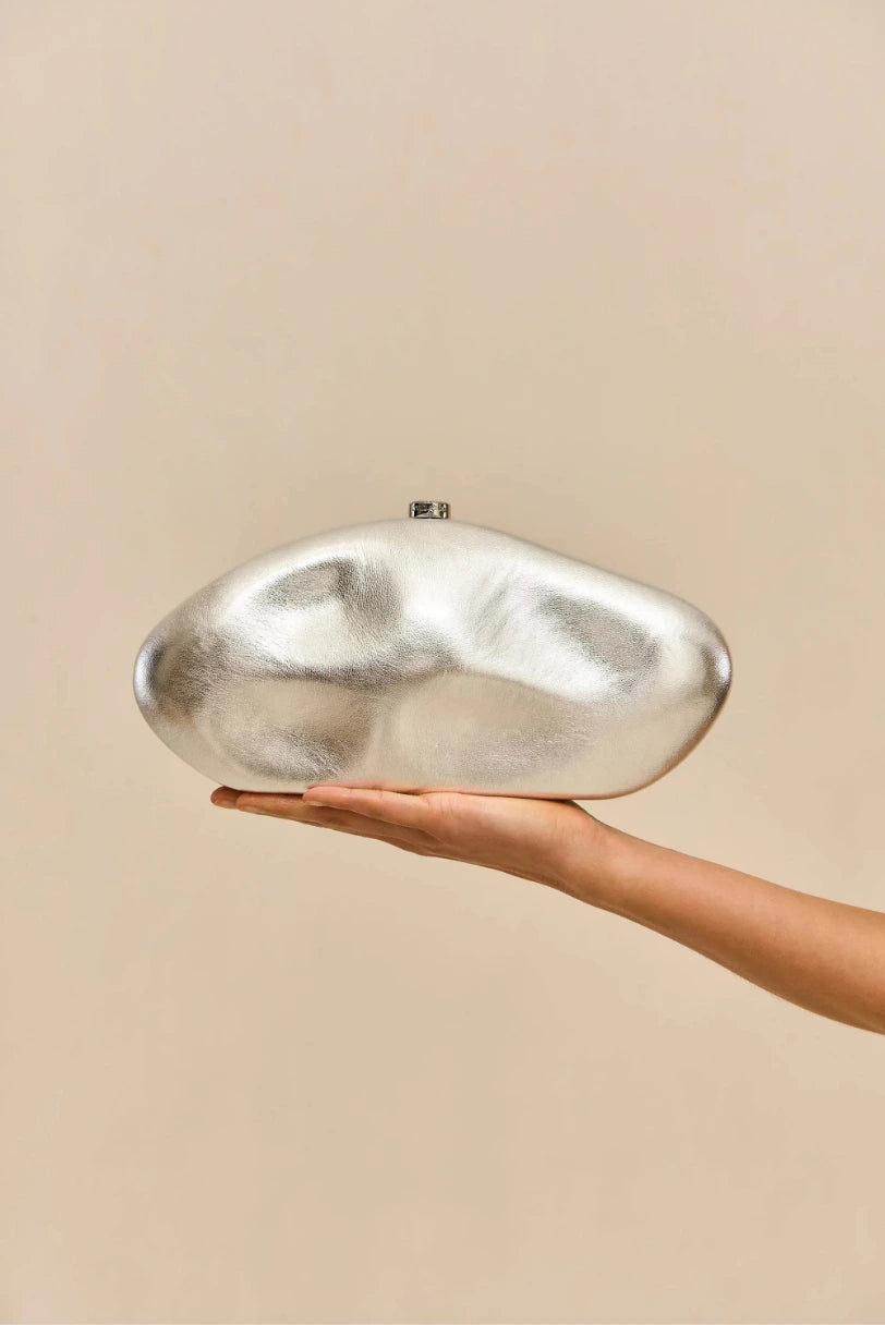 Modelo segurando a Clutch Caldera Cult Gaia prata na palma da mao